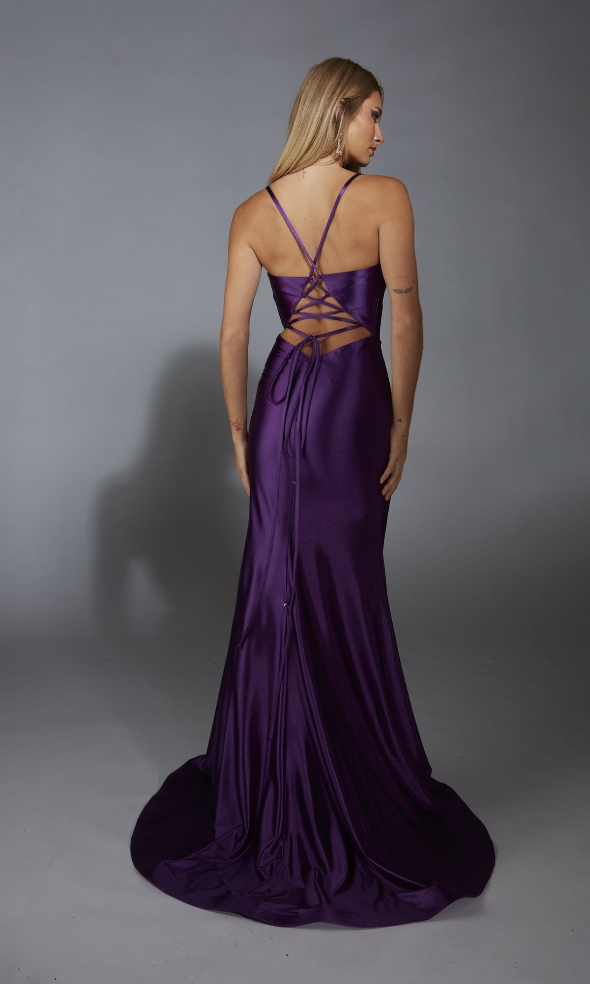 A woman models the Lace-Up Open-Back Long Prom Dress: Aerie Couture 313, featuring a floor-length purple satin design and striking back detail, as she stands facing away against a plain gray background.